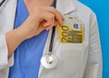 Woman doctor puts Euro bills in her pocket, close-up. Nurse in medical gown with money, blue background