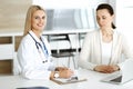 Woman-doctor sitting and communicating with her female patient in clinic. Blonde physician happy to help. Medicine