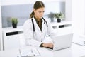 Woman-doctor typing on laptop computer while sitting at the desk in hospital office. Physician at work. Data in medicine Royalty Free Stock Photo
