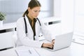 Woman-doctor typing on laptop computer while sitting at the desk in hospital office. Physician at work. Data in medicine Royalty Free Stock Photo