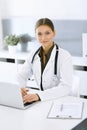 Woman-doctor typing on laptop computer while sitting at the desk in hospital office. Physician at work. Data in medicine Royalty Free Stock Photo