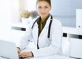 Woman-doctor typing on laptop computer while sitting at the desk in sunny hospital office. Physician at work Royalty Free Stock Photo