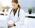 Woman-doctor typing on laptop computer while sitting at the desk in sunny hospital office. Physician at work Royalty Free Stock Photo