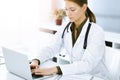 Woman-doctor typing on laptop computer while sitting at the desk in sunny hospital office. Physician at work Royalty Free Stock Photo