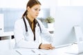 Woman-doctor typing on pc computer while sitting at the desk in hospital office. Physician at work Royalty Free Stock Photo