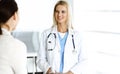 Woman-doctor at work in hospital is happy to communicate with female patient. Blonde physician checks medical history