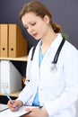 Woman doctor at work at hospital. Young female physician write prescription or filling up medical form while sitting in Royalty Free Stock Photo