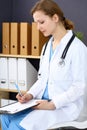 Woman doctor at work at hospital. Young female physician write prescription or filling up medical form while sitting in Royalty Free Stock Photo