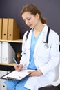 Woman doctor at work at hospital. Young female physician write prescription or filling up medical form while sitting in Royalty Free Stock Photo