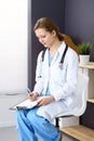 Woman doctor at work at hospital. Young female physician write prescription or filling up medical form while sitting in Royalty Free Stock Photo