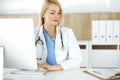 Woman-doctor at work while sitting at the desk in hospital or clinic. Blonde cheerful physician using desktop computer Royalty Free Stock Photo