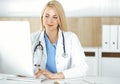 Woman-doctor at work while sitting at the desk in hospital or clinic. Blonde cheerful physician using desktop computer Royalty Free Stock Photo