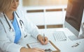 Woman-doctor at work while sitting at the desk in sunny clinic. Blonde cheerful physician filling up medication history