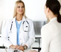 Woman-doctor at work in sunny hospital is happy to consult female patient. Blonde physician checks medical history