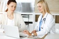 Woman-doctor at work in sunny hospital is happy to consult female patient. Blonde physician checks medical history