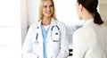 Woman-doctor at work in sunny hospital is happy to consult female patient. Blonde physician checks medical history