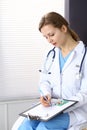 Woman doctor write prescription while sitting in hospital office. A lot of various colored pills liye at her clipboard Royalty Free Stock Photo