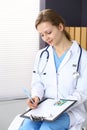 Woman doctor write prescription while sitting in hospital office. A lot of various colored pills liye at her clipboard Royalty Free Stock Photo