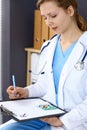 Woman doctor write prescription while sitting in hospital office. A lot of various colored pills liye at her clipboard Royalty Free Stock Photo