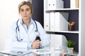 Woman doctor write prescription while sitting in hospital office. A lot of various colored pills liye at her clipboard Royalty Free Stock Photo