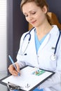 Woman doctor write prescription while sitting in hospital office. A lot of various colored pills liye at her clipboard Royalty Free Stock Photo