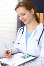 Woman doctor write prescription while sitting in hospital office. A lot of various colored pills liye at her clipboard Royalty Free Stock Photo