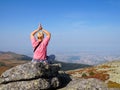 A woman does yoga on the top of a mountain, at the foot of which there is a large metropolis