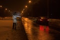 A woman with a dog catches a car on the road at night in winter