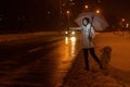 A woman with a dog catches a car on the road at night in winter