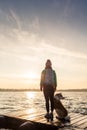 Woman with dog enjoy sunrise at lake, backpacker silhouette