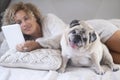 Woman and dog laying on the bed. Happy female people reding with ebook reader and having relax with her best friend old dog pug. Royalty Free Stock Photo