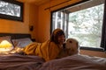 Woman with a dog lying on bed at wooden cabin on nature