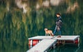 Woman dog owner and his friend beagle dog on the wooden pier on the mountain lake during their walking in the autumn season time.
