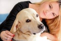 Woman with dog is resting in bed at home, relaxing in bedroom. Girl is petting with her dog. Portrait of cute yellow labrador.