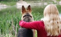 A woman with a dog sits on the shore of the lake. German shepherd and blonde girl for a walk. View from the back Royalty Free Stock Photo