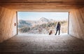 Woman with dog stay in big wooden hangar and looks on snowy mountains
