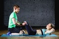 Woman doing abdominal crunches press exercise on the mat with her sports male trainer in gym. Royalty Free Stock Photo