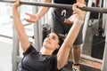Woman Doing Bench Press While Instructor Assisting Her In Gym