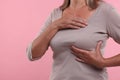 Woman doing breast self-examination on pink background, closeup