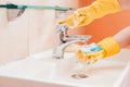 woman doing chores in bathroom at home, cleaning surfaces sink and faucet with spray detergent suds sponge. Royalty Free Stock Photo