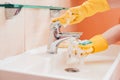 woman doing chores in bathroom at home, cleaning surfaces sink and faucet with spray detergent suds sponge. Royalty Free Stock Photo