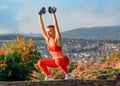 Woman doing dumbbell exercises in the park against city