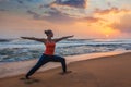 Woman doing yoga asana Virabhadrasana 1 Warrior Pose on beach on