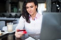 Woman doing online shopping at cafe, holding credit card typing numbers on laptop computer.