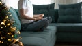 Woman doing online shopping at Christmas: she is sitting on the sofa at home, connecting with her laptop. Christmas tree in the Royalty Free Stock Photo