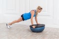 Woman doing plank for abdominal muscles on bosu balance trainer, holding balance on fitness ball. Royalty Free Stock Photo