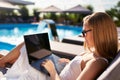 Woman doing remote multitasking work with multiple electronic internet devices on swimming pool beach bed. Freelancer