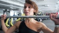 Woman is doing set of reps exercise with barbell lifting it over the head in gym.