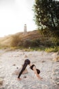 Young Woman Practicing yoga in the nature at sunset on sand beach against of lighthouse. Downward Facing Dog Pose Adho Mukha Royalty Free Stock Photo