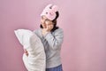 Woman with down syndrome wearing sleeping mask hugging pillow looking stressed and nervous with hands on mouth biting nails Royalty Free Stock Photo